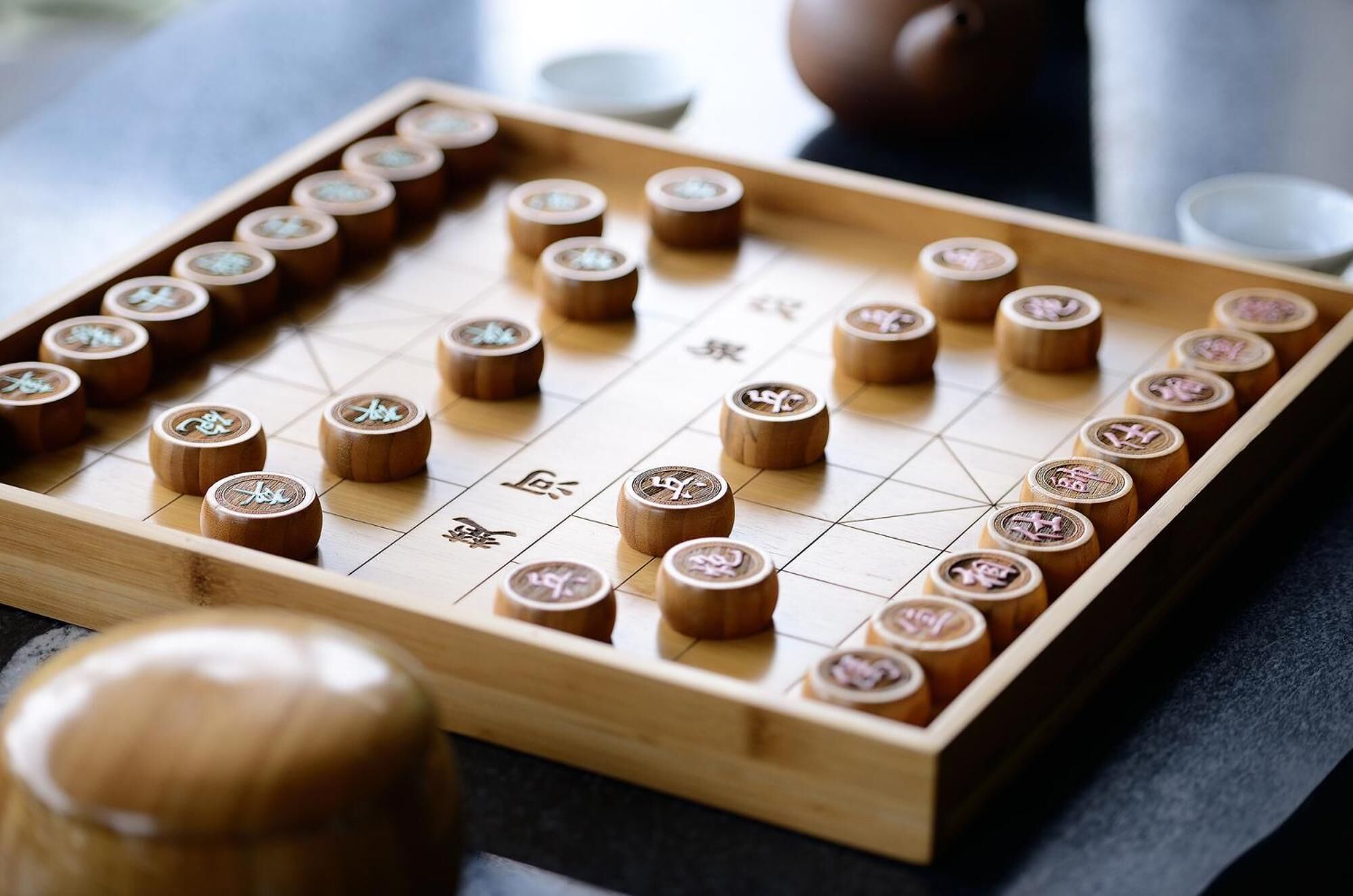 A Go board with pieces and a wooden bowl.