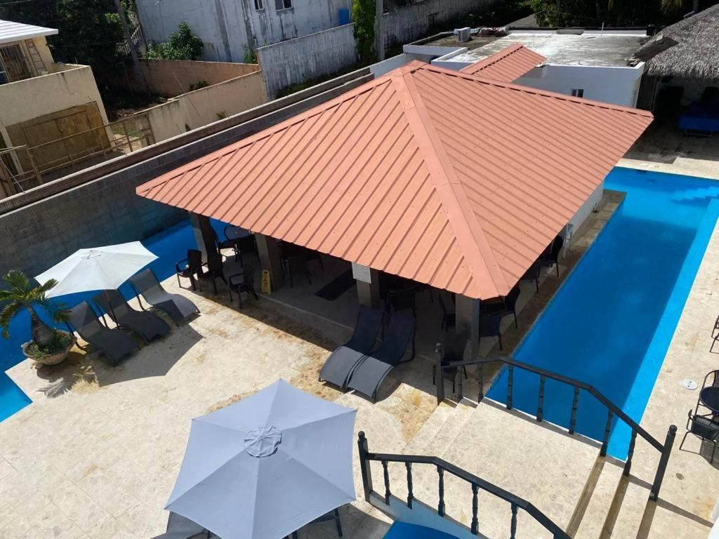 A rooftop pool area with a red roof, lounge chairs, and umbrellas.