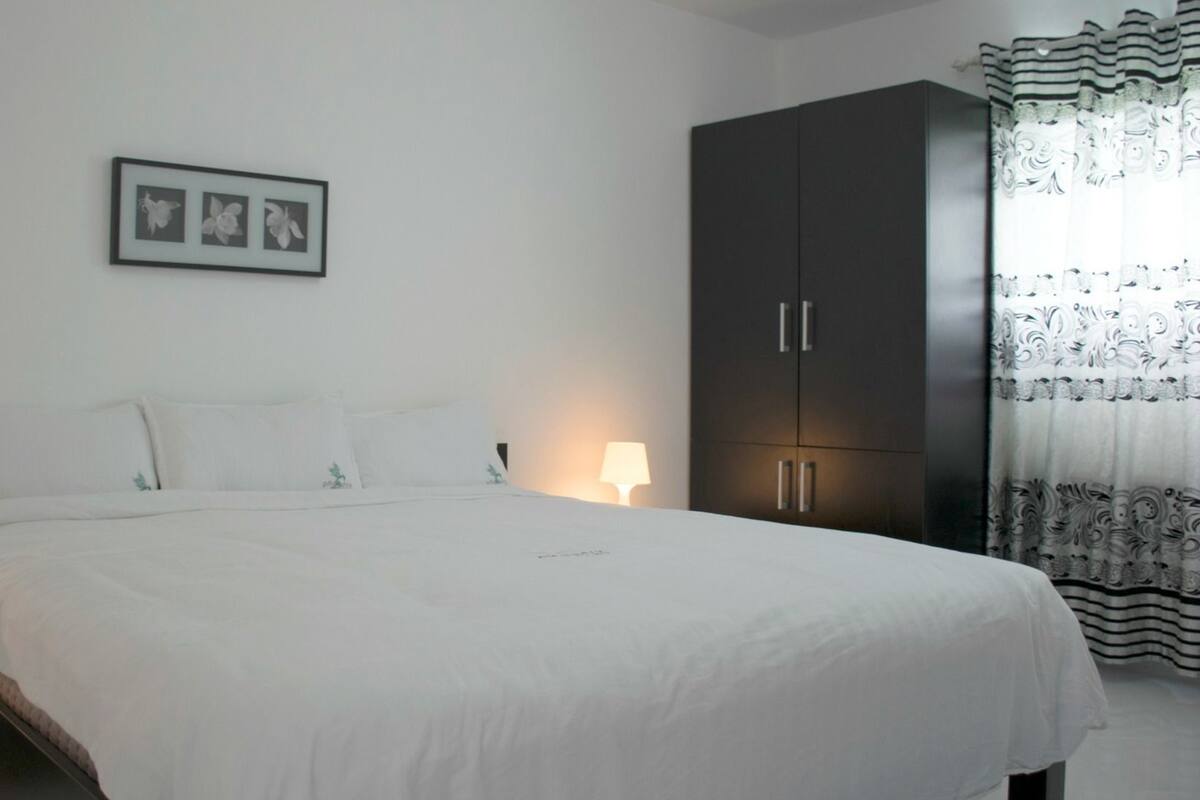 A bedroom with a large bed, a wardrobe, a nightstand, and a lamp.
