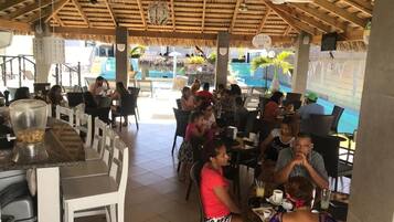 Un área de comedor al aire libre con mesas y sillas, una barra y una piscina al fondo.