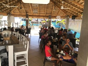 An outdoor dining area with tables and chairs, a bar area, and a pool in the background. - El Cabarete Spa & Resort (Cabarete)