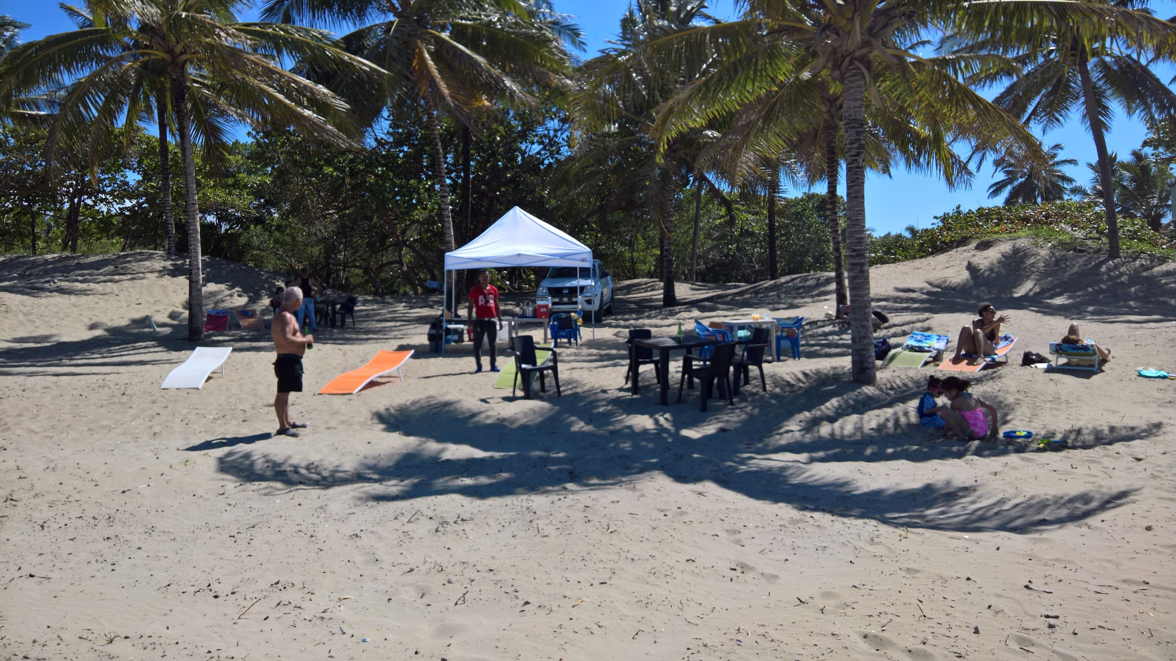 A beach with a tent, tables, chairs, and people.
