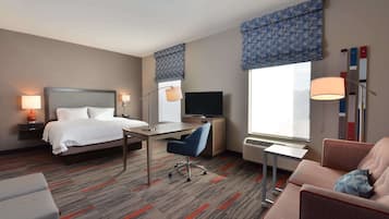 Habitación de hotel con cama, escritorio, silla, sofá, televisión y ventana grande.