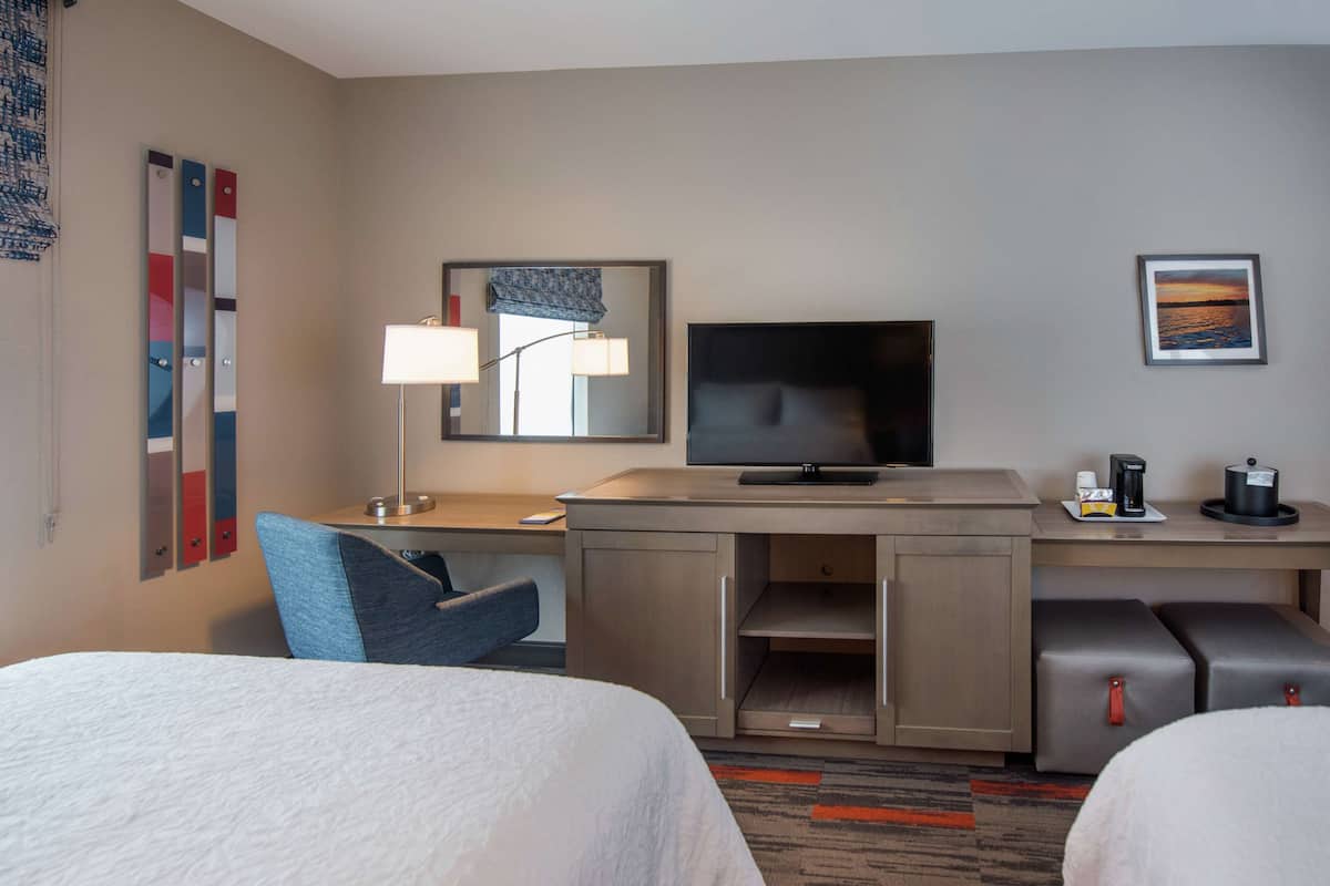 A hotel room with two beds, a desk with a TV, a lamp, and a coffee maker.