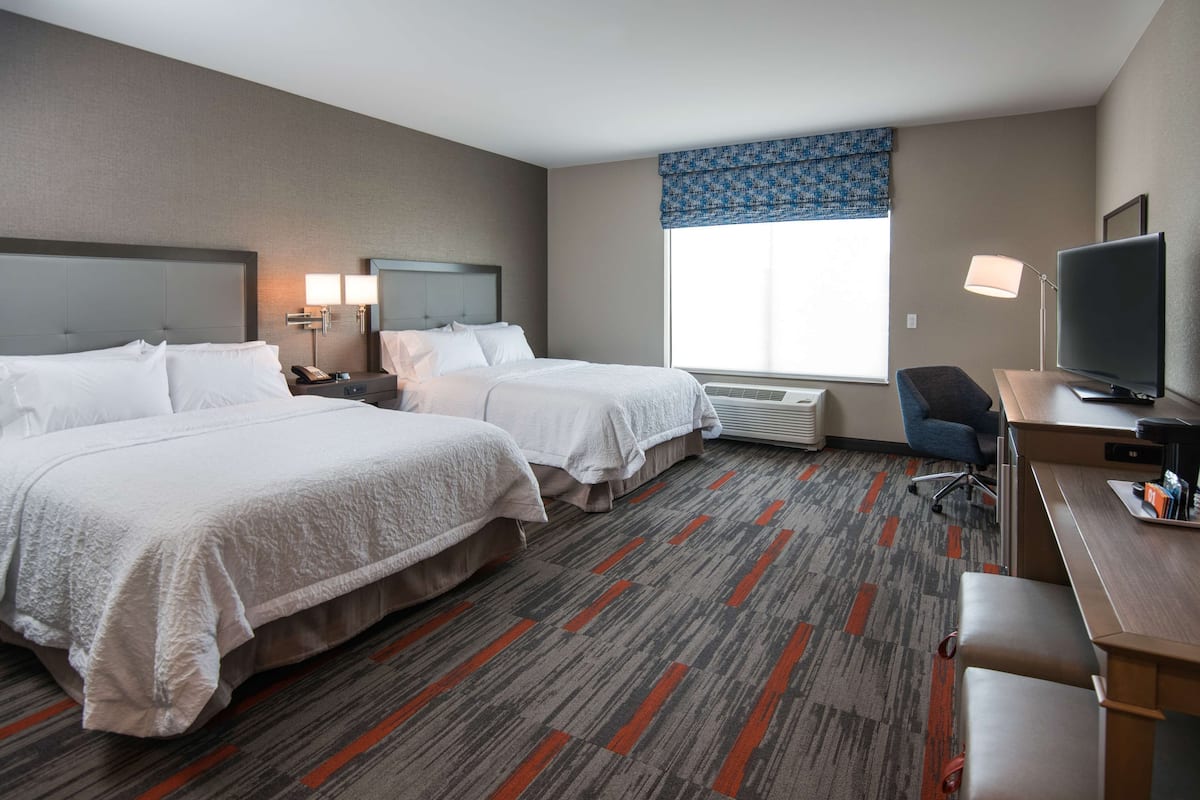 A hotel room with two beds, a desk, a chair, a TV, and a window with a blue valance.