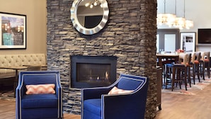 A cozy room with a stone fireplace, two blue armchairs with cushions, a round mirror, and a dining area in the background. - Hampton Inn & Suites at Wisconsin Dells Lake Delton (Baraboo)