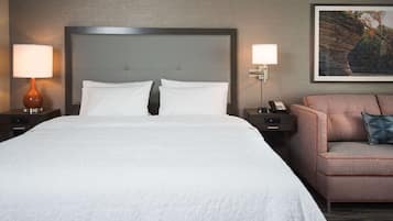 A hotel room with a large bed, two bedside tables with lamps, a nightstand with a phone, a sofa with a pillow, and a framed picture on the wall.