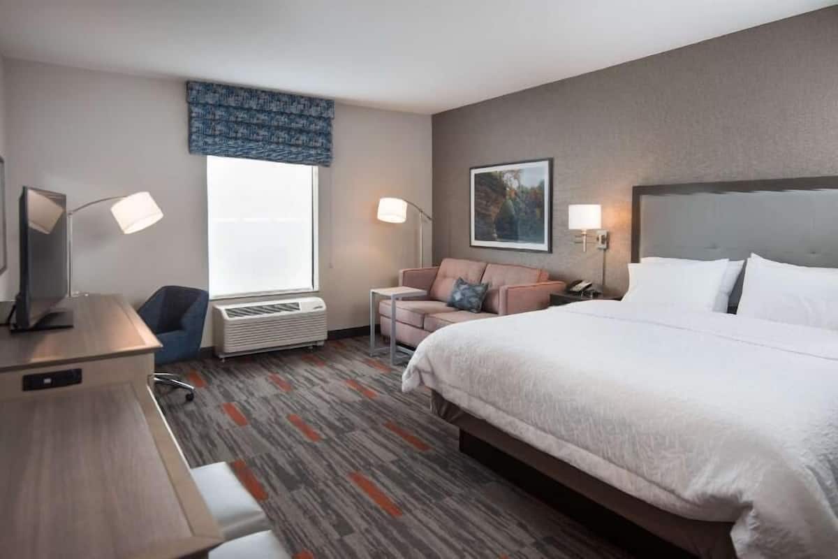 A hotel room with a bed, desk, chair, and a window with a view.