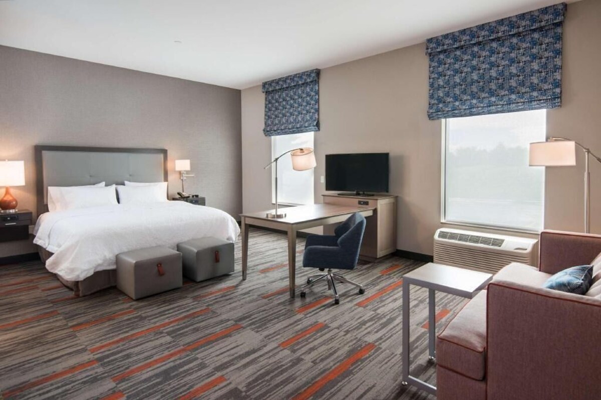 A hotel room with a bed, desk, chair, and a TV.