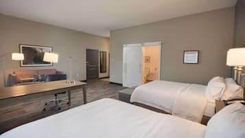 Une chambre d’hôtel avec deux lits, un bureau avec une chaise, un canapé et une porte donnant sur une salle de bain.