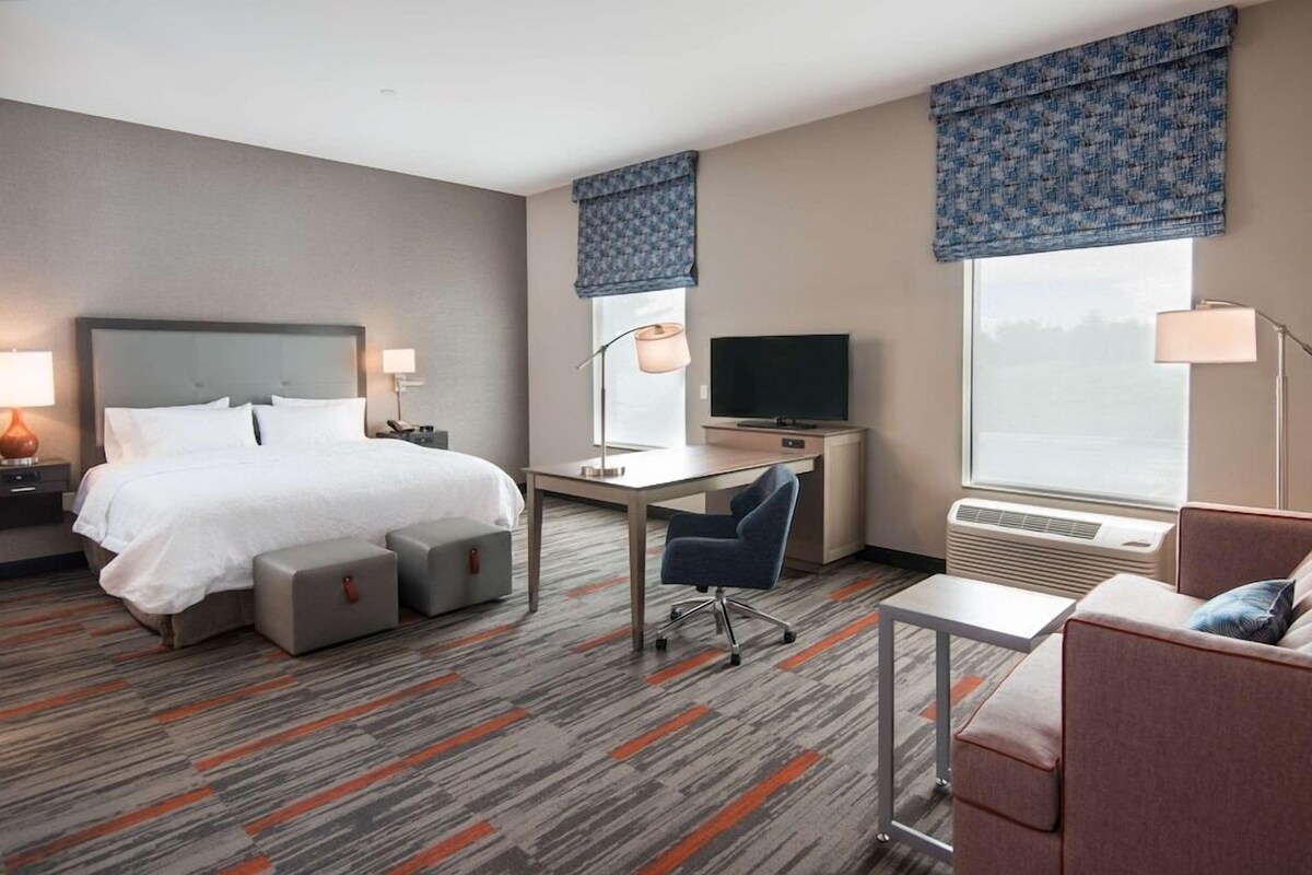 A hotel room with a bed, desk, chair, and a television.