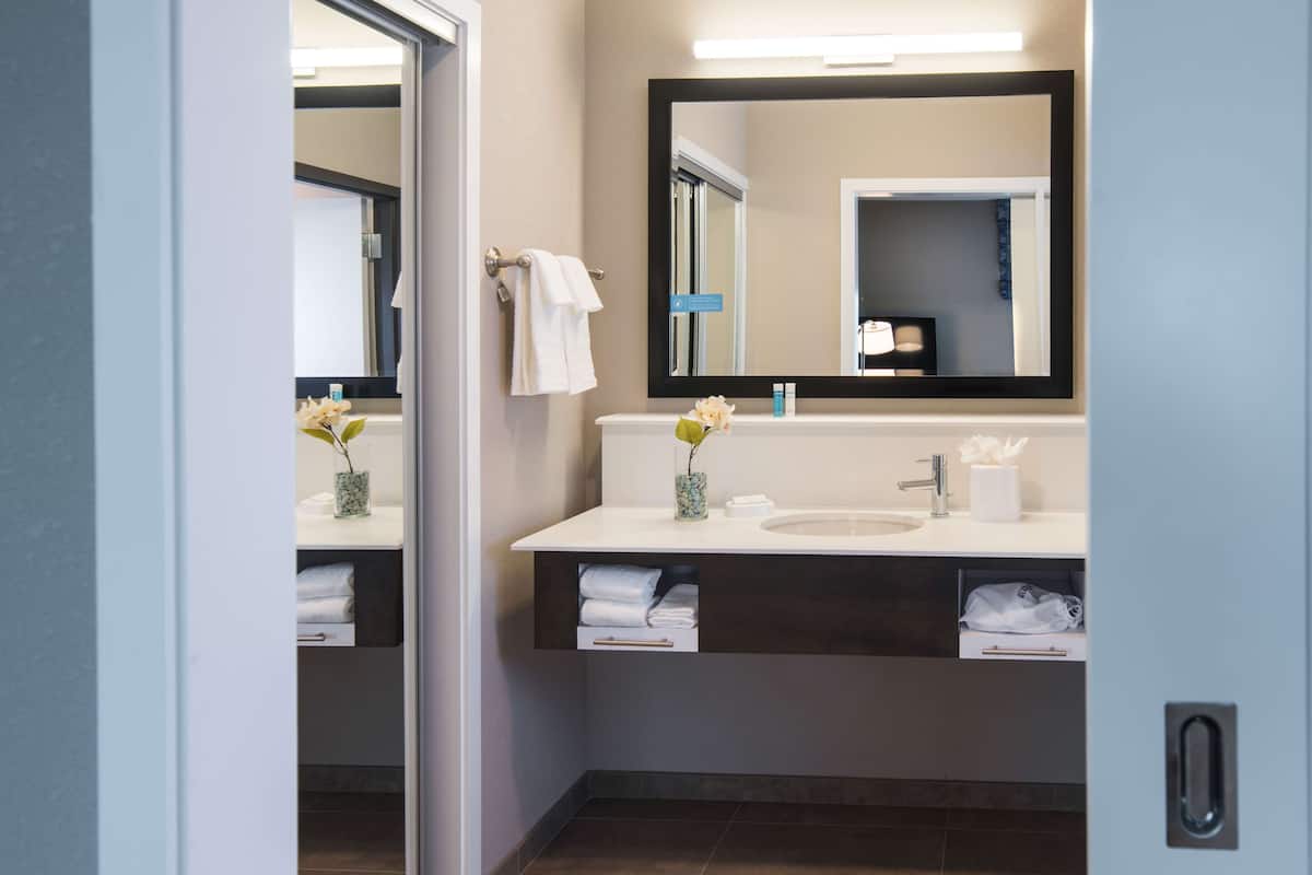 A modern bathroom with a white sink, a large mirror, and a towel rack.