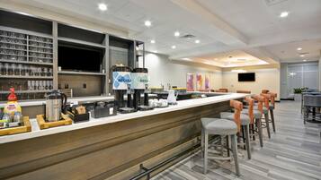 Un'area bar moderna con un lungo bancone, sgabelli e una postazione caffè.