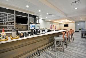 Un área de bar moderna con una barra larga, taburetes y una estación de café.