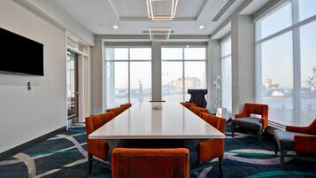 A conference room with a long table, orange chairs, large windows, and a flat-screen TV on the wall.