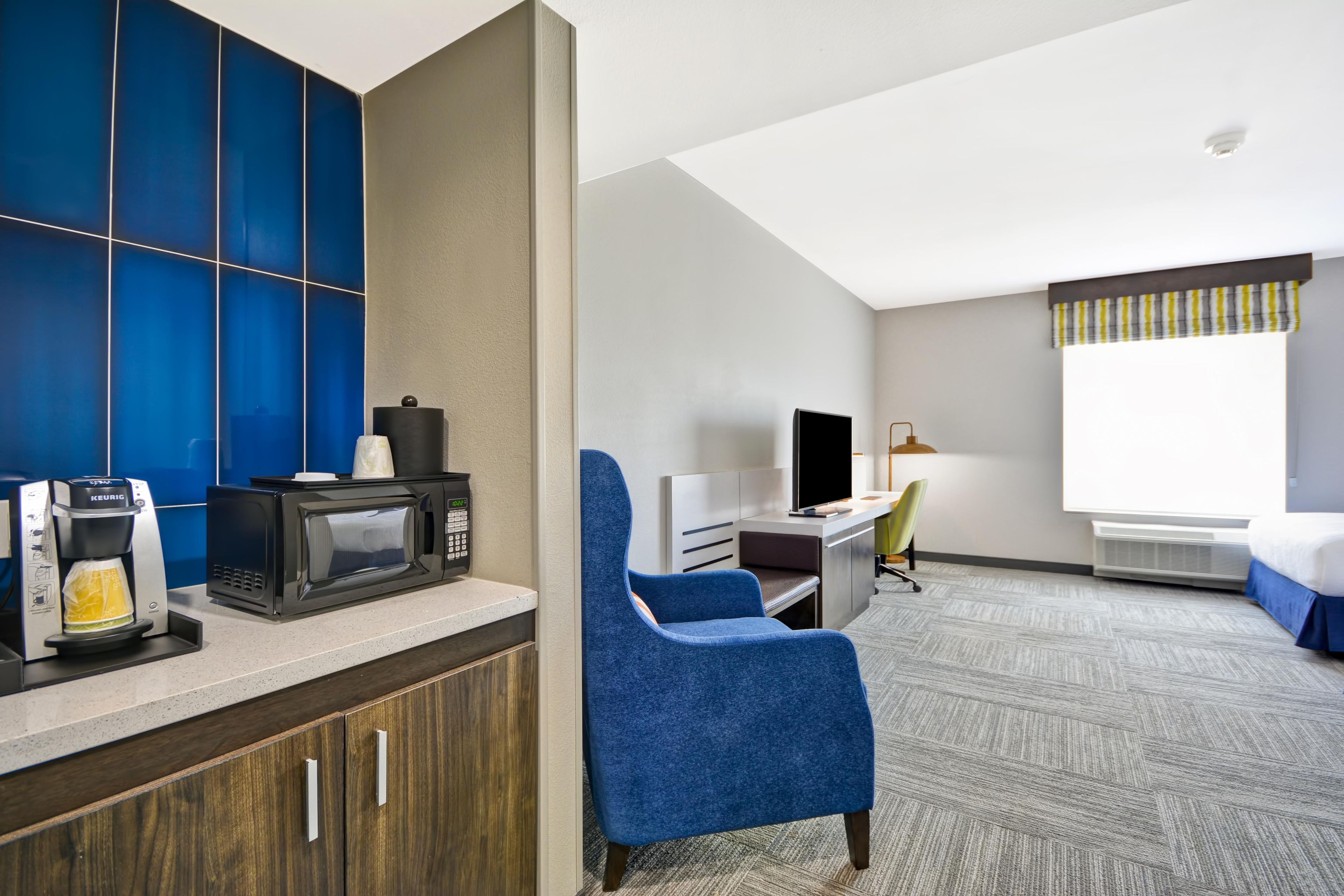 Ein Hotelzimmer mit einer Küchenzeile, einem Schreibtisch, einem Stuhl, einem Bett und einem großen Fenster.