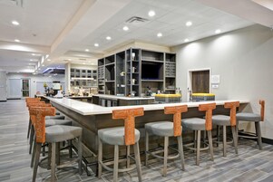 Zona de bar moderna con mostrador, taburetes y una cocina al fondo.