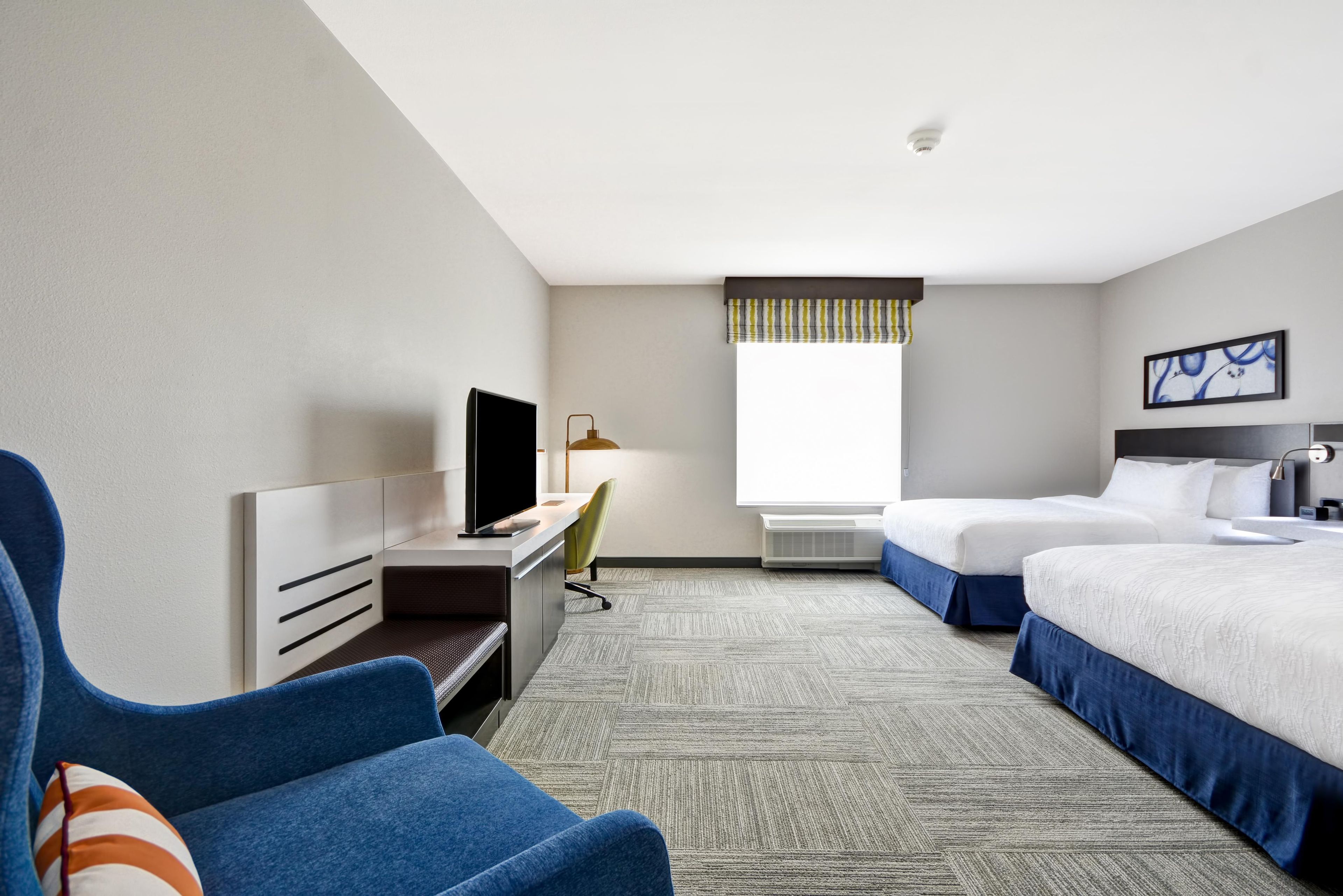A hotel room with a bed, a desk with a TV, a chair, and a window with a view.