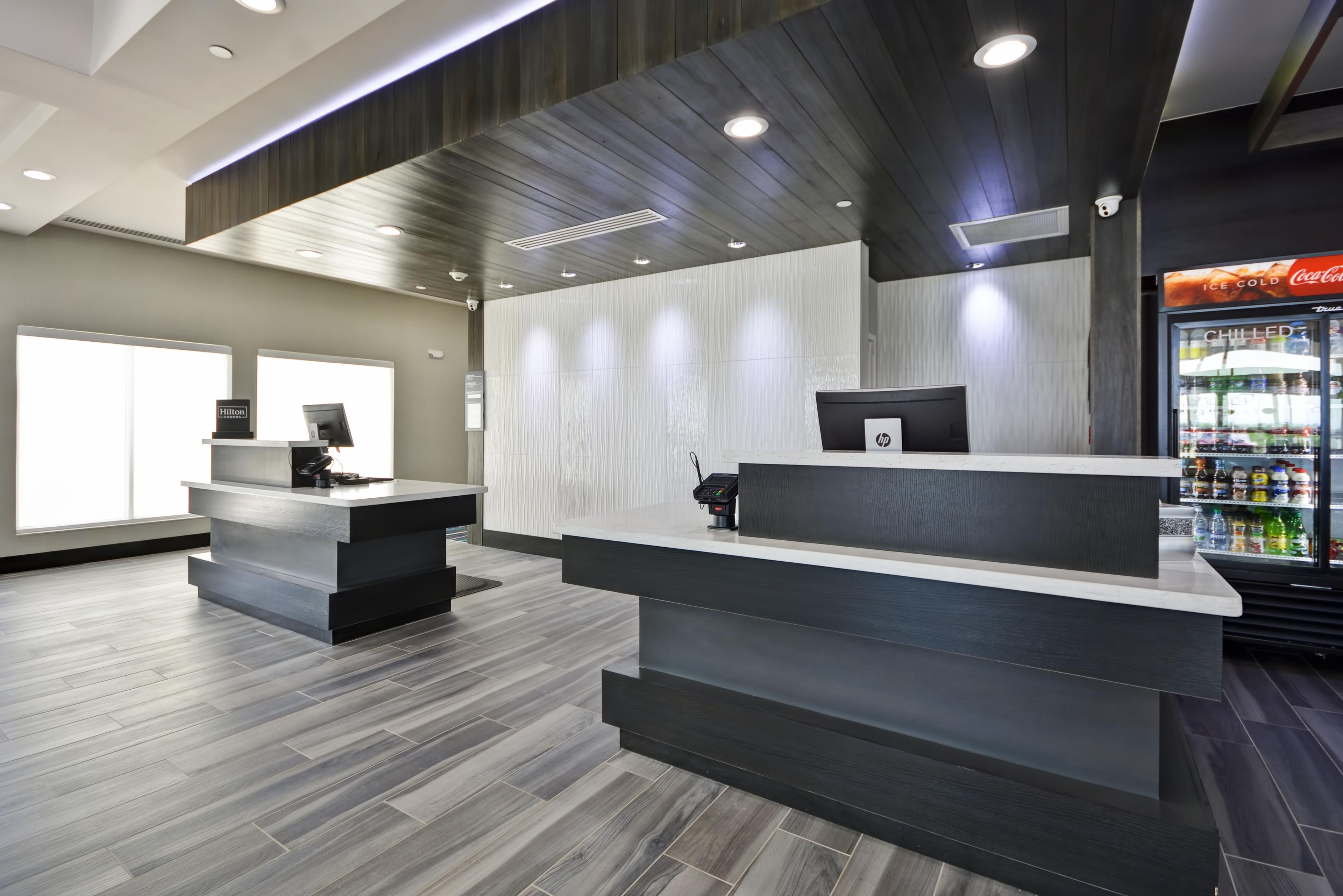 A hotel reception area with a modern design, featuring a reception desk, a computer, and a Coca-Cola refrigerator.