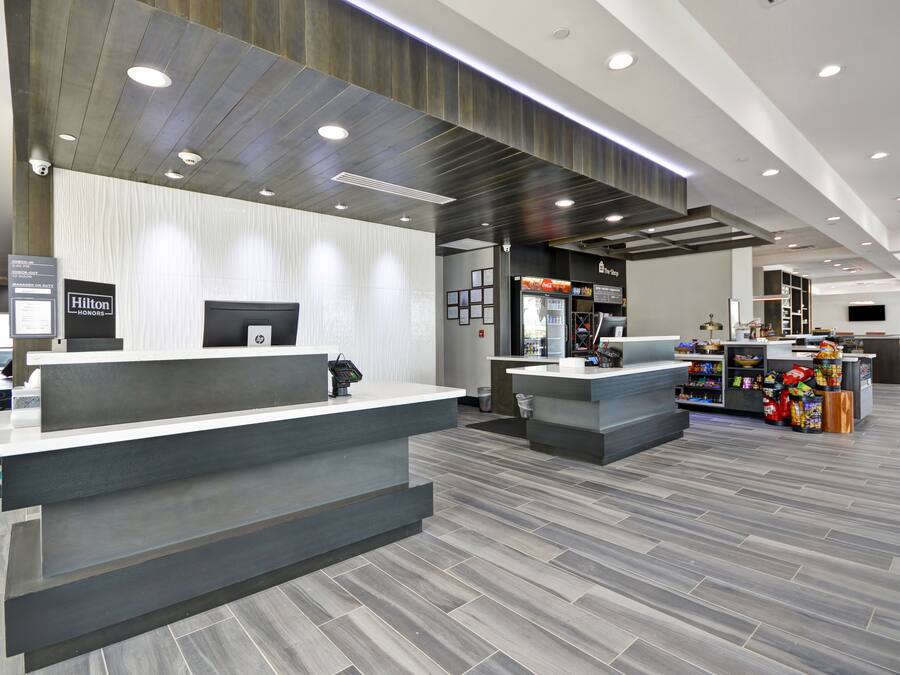A modern hotel reception area with a grey reception desk, a digital display, and a food kiosk.