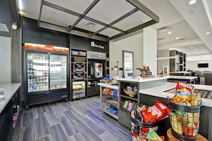 Un espacio comercial moderno con un expositor refrigerado, contenedores para aperitivos y un mostrador con un letrero que dice "The Shop".