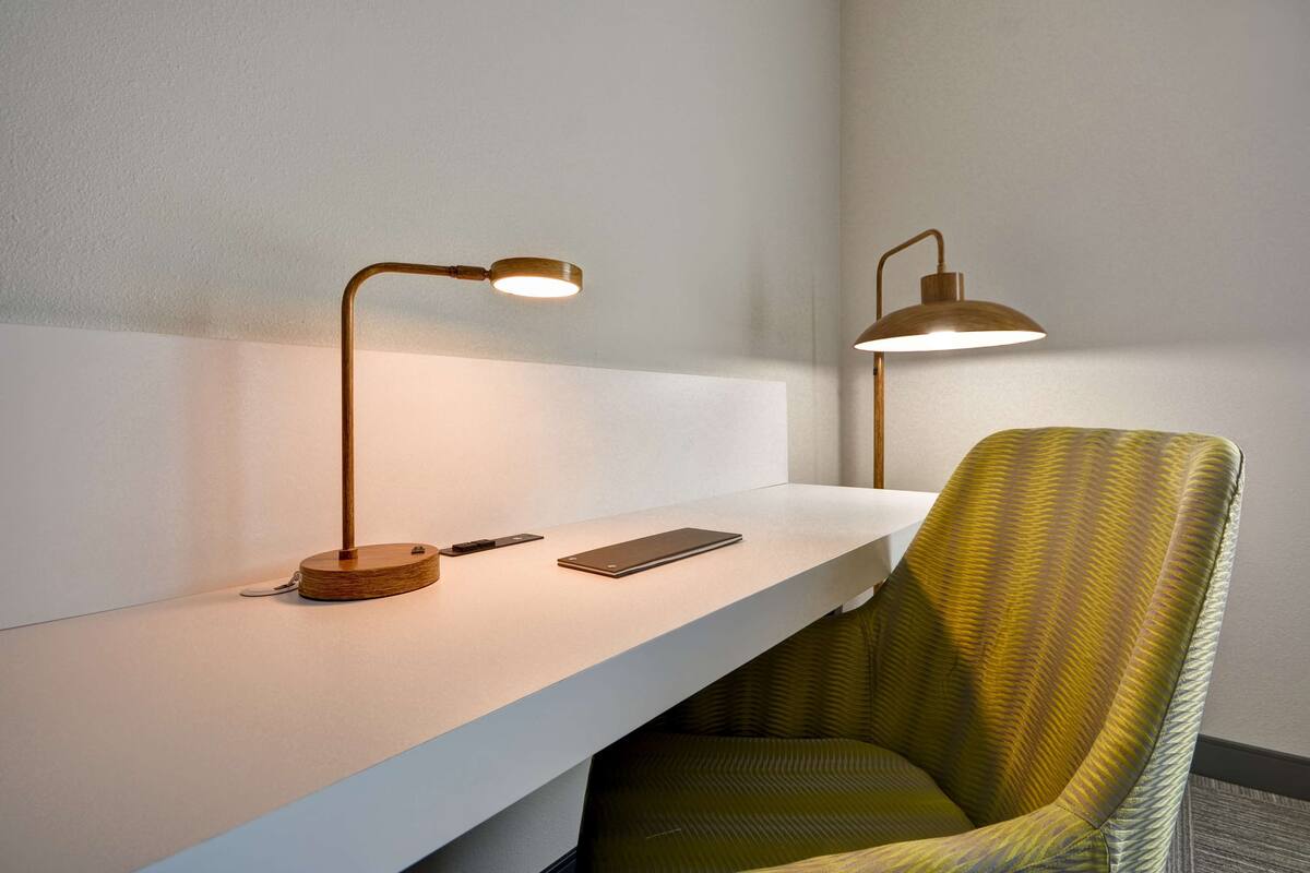 A modern desk with a laptop, a smartphone, and a wooden desk lamp.