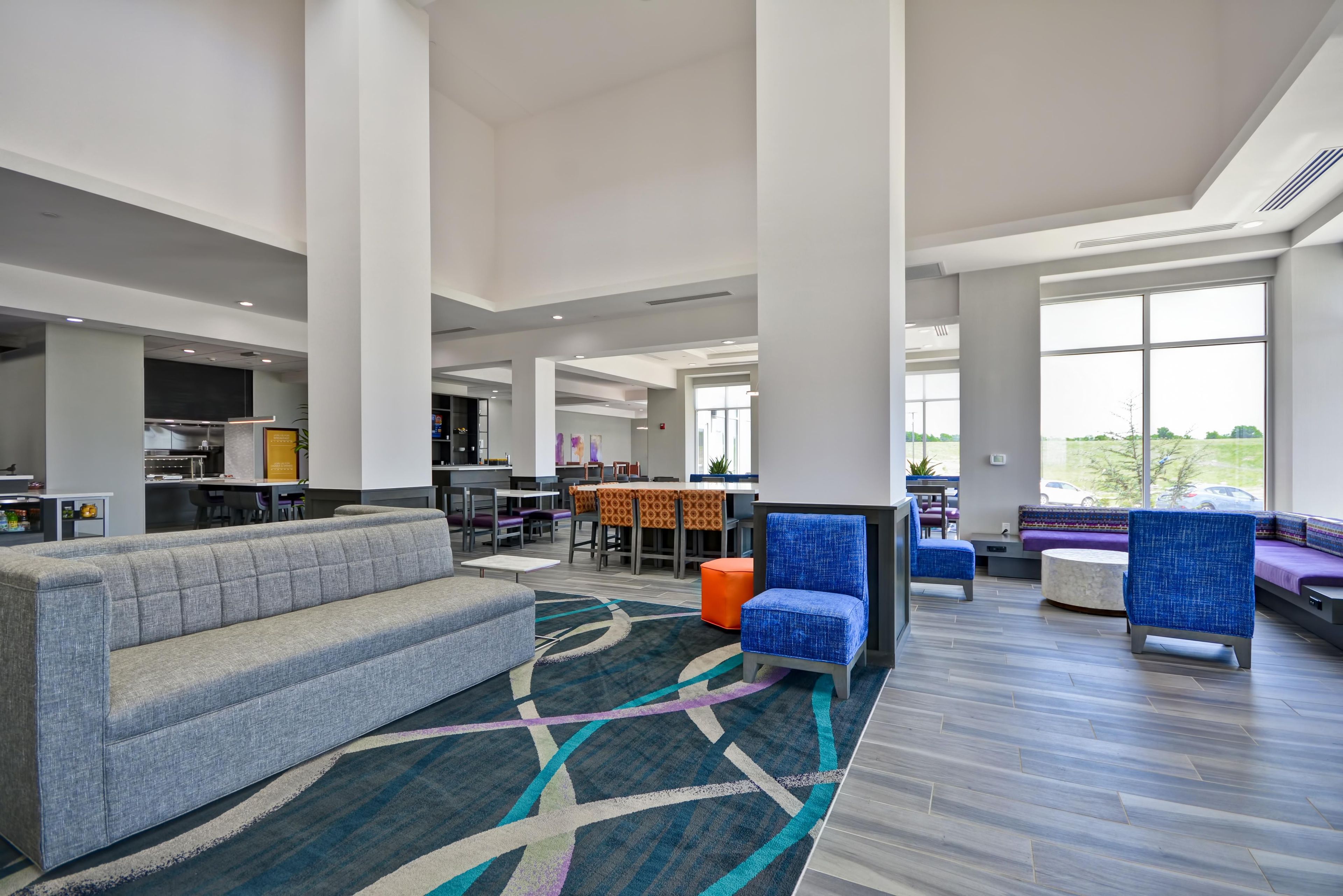 Un hall d’entrée spacieux, avec un canapé gris, des fauteuils bleus et un tapis à motifs.