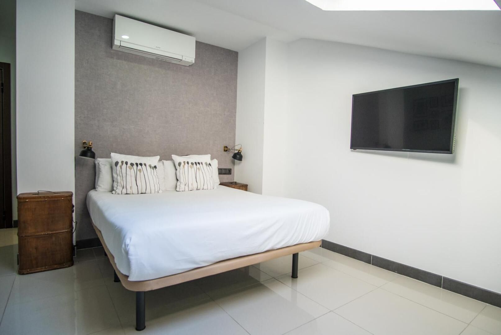 A modern bedroom with a large bed, a flat-screen TV mounted on the wall, and a ceiling fan.