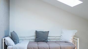 Una cama con estructura metálica blanca, colchón color beige y tres almohadas en tonos grises y blancos.