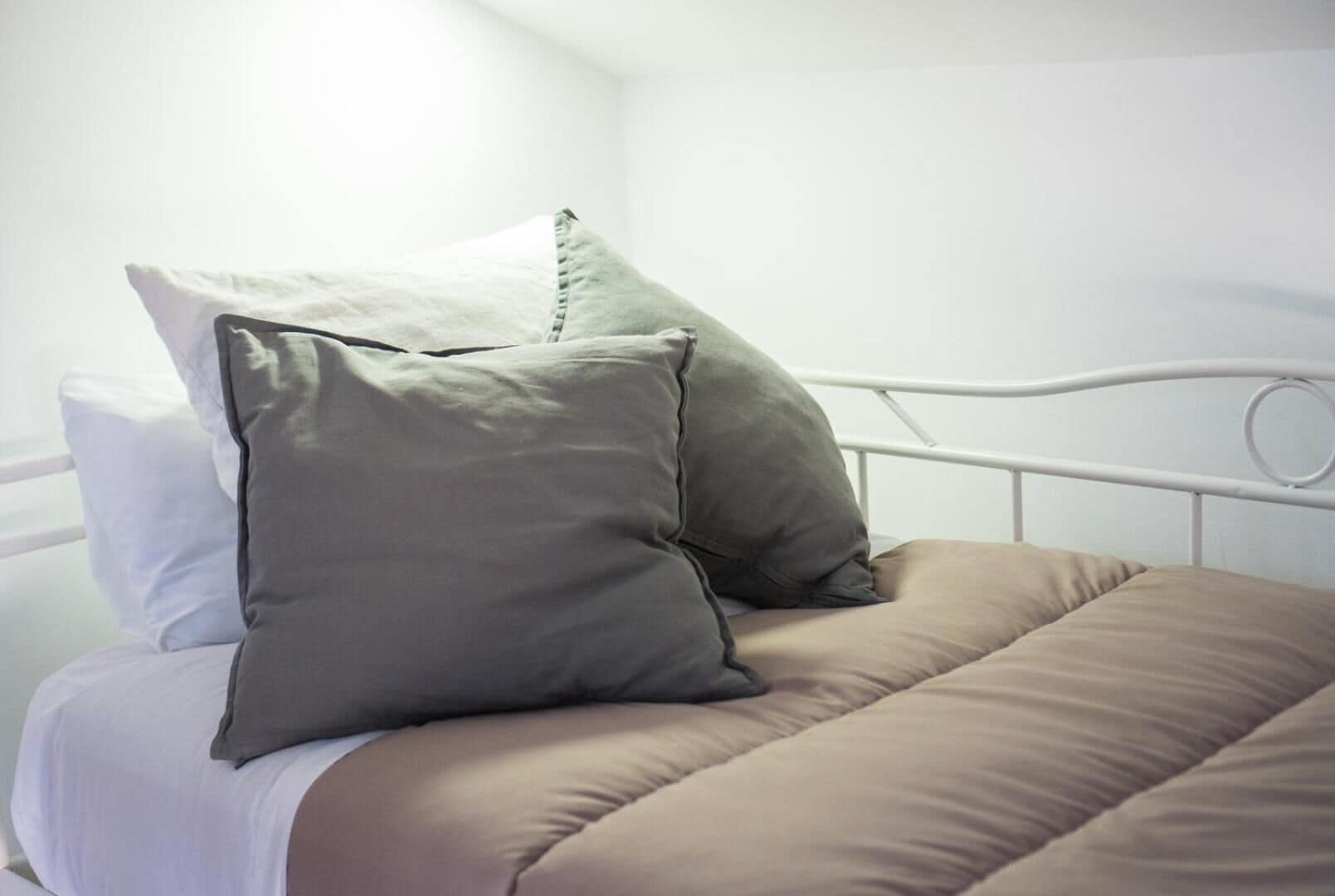 Un lit avec un cadre en métal blanc, une couvre-lit beige et deux oreillers, un blanc et un gris.