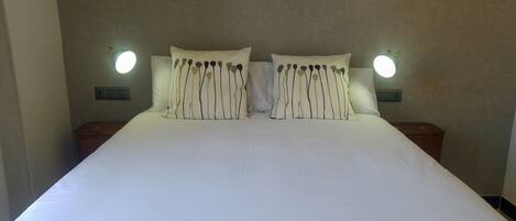A neatly made bed with white linens and striped pillows, flanked by two bedside tables with wall-mounted lamps.