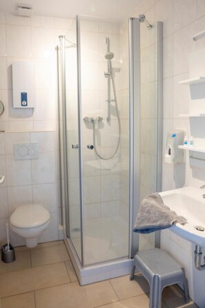 Un baño moderno con ducha de vidrio, inodoro, lavamanos y un taburete.