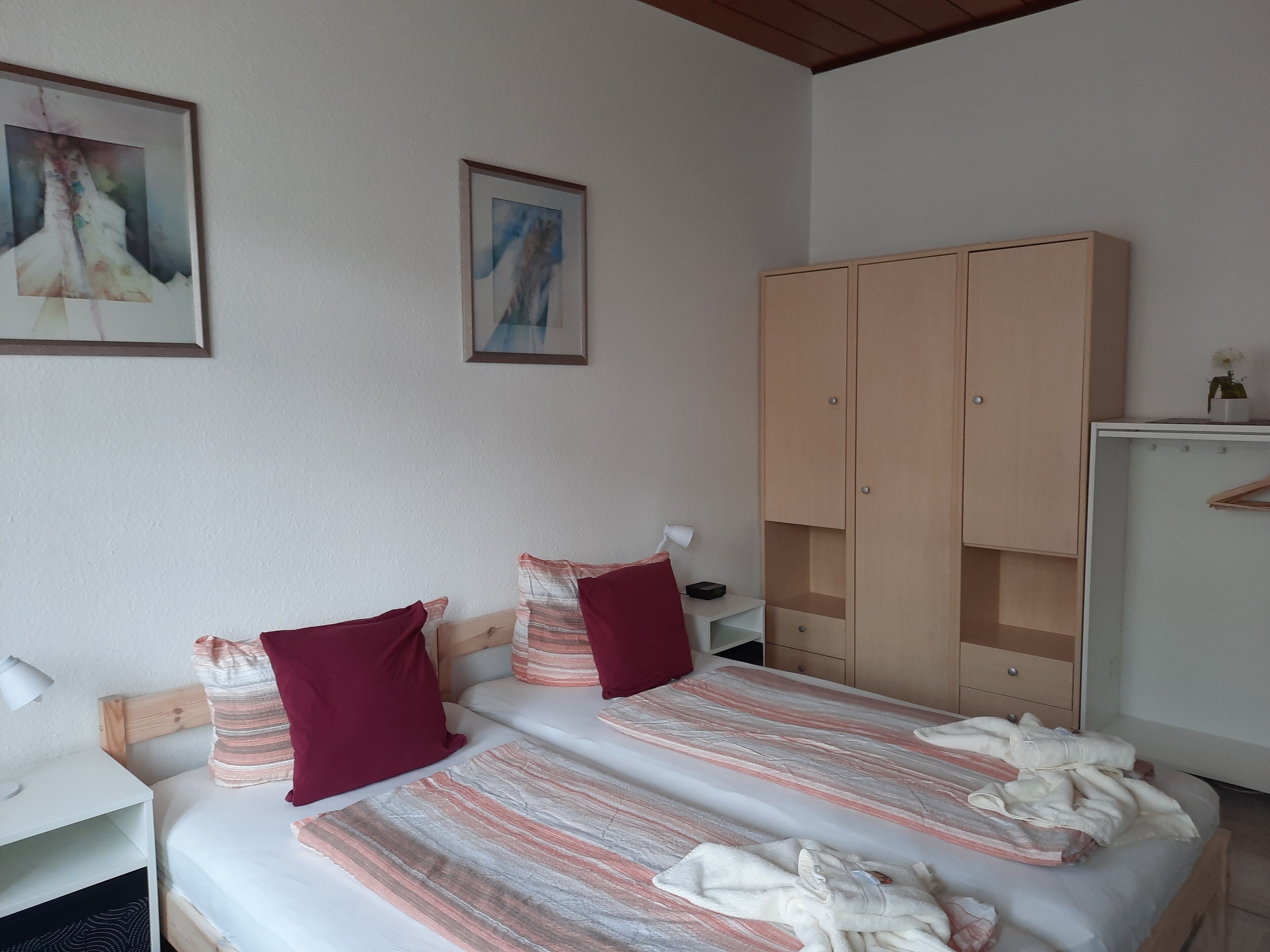 Une chambre à coucher avec un lit, deux oreillers, une table de chevet, une lampe, une armoire et deux tableaux encadrés accrochés au mur.