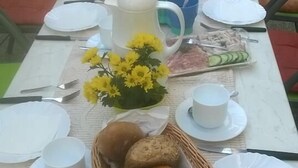 Une table à manger dressée avec des assiettes, des couverts, un pichet, un panier de pain et un vase de fleurs.