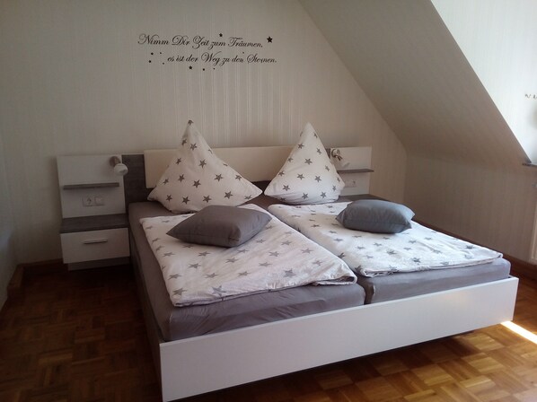Un dormitorio con techo inclinado, una cama con cabecera blanca, dos mesitas de noche y una pared con inscripción de motivos estelares.