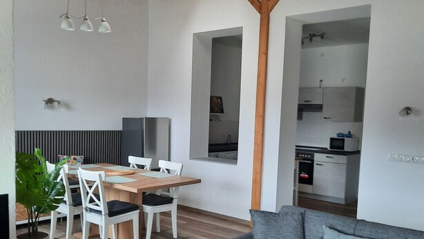 Un espace de vie moderne comprenant un coin repas, un canapé gris, un plancher en bois et des poutres apparentes.