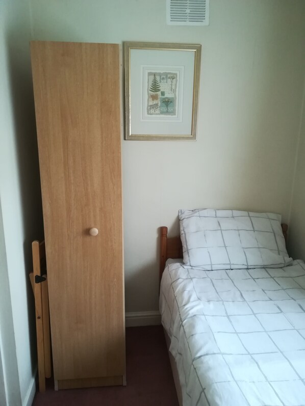 Une chambre à coucher avec une armoire en bois, un lit recouvert d’une couette blanche et un tableau encadré accroché au mur.