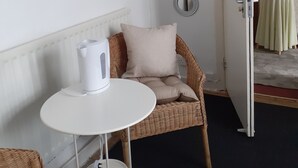 Et værelse med en hvid radiator, en fletstol med pude, et lille hvidt bord med elkedel og tre spejle på væggen.