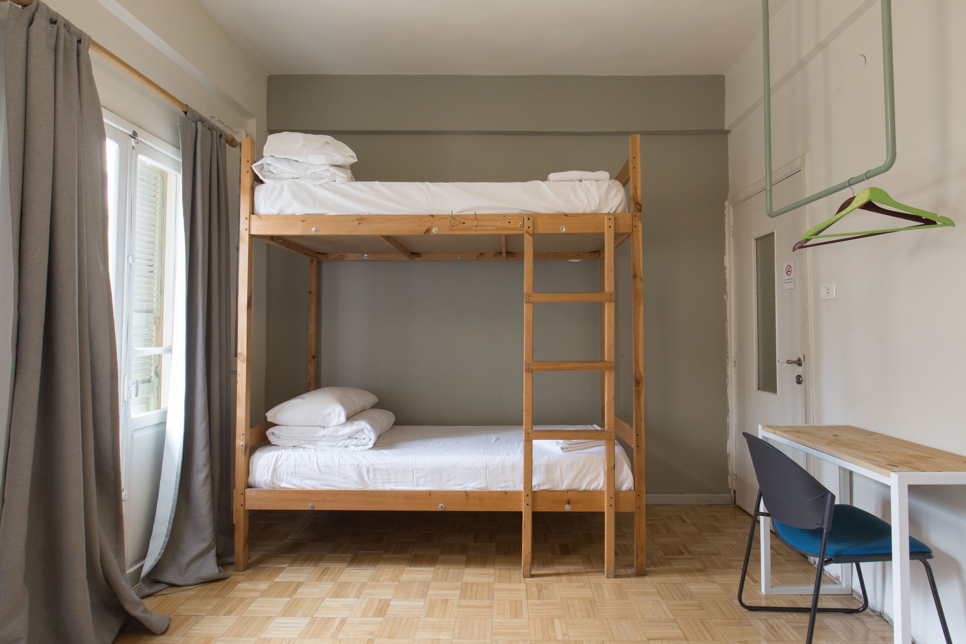 Ein Stockbett mit Schreibtisch, Stuhl, einer Leiter und einem Fenster mit Vorhängen.