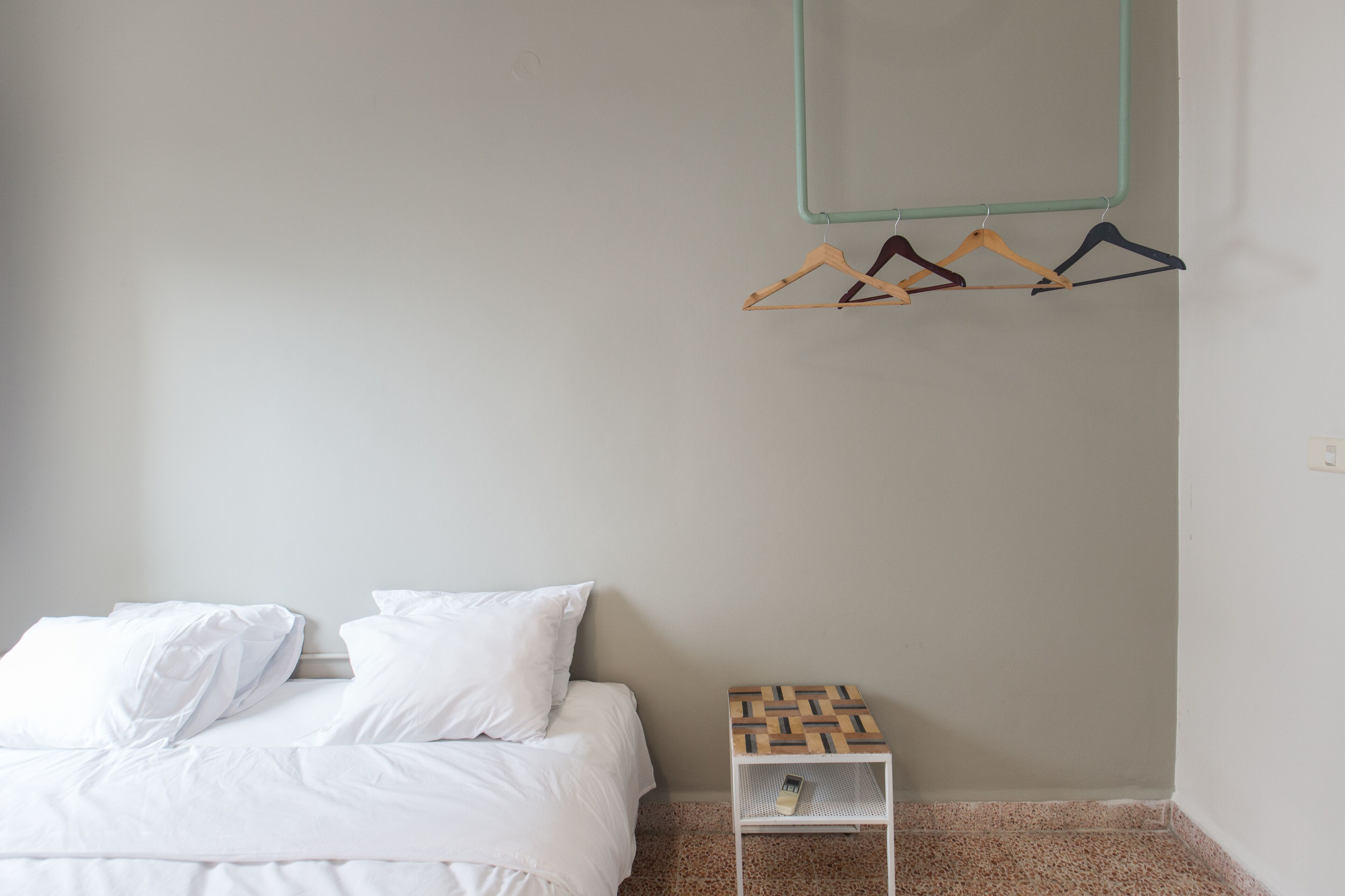 Une chambre à coucher avec un lit, des oreillers blancs, une table de chevet en bois et un porte-manteau mural avec des cintres.