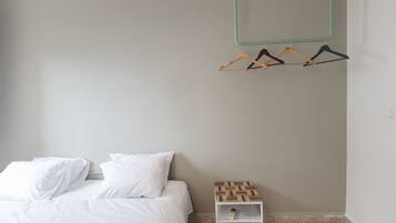 Une chambre à coucher avec un lit, des oreillers blancs, une table de chevet en bois et un porte-manteau mural avec des cintres.