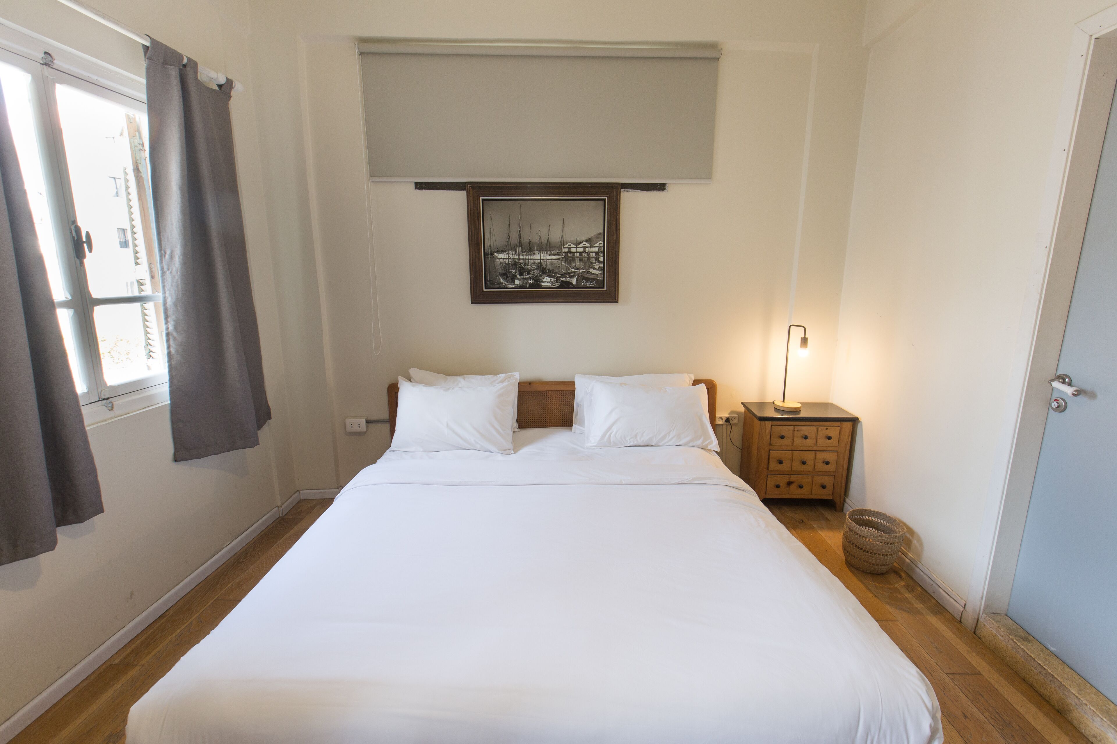 Un dormitorio con una cama grande, una mesita de noche, una lámpara, un cuadro en la pared y una ventana con cortinas.
