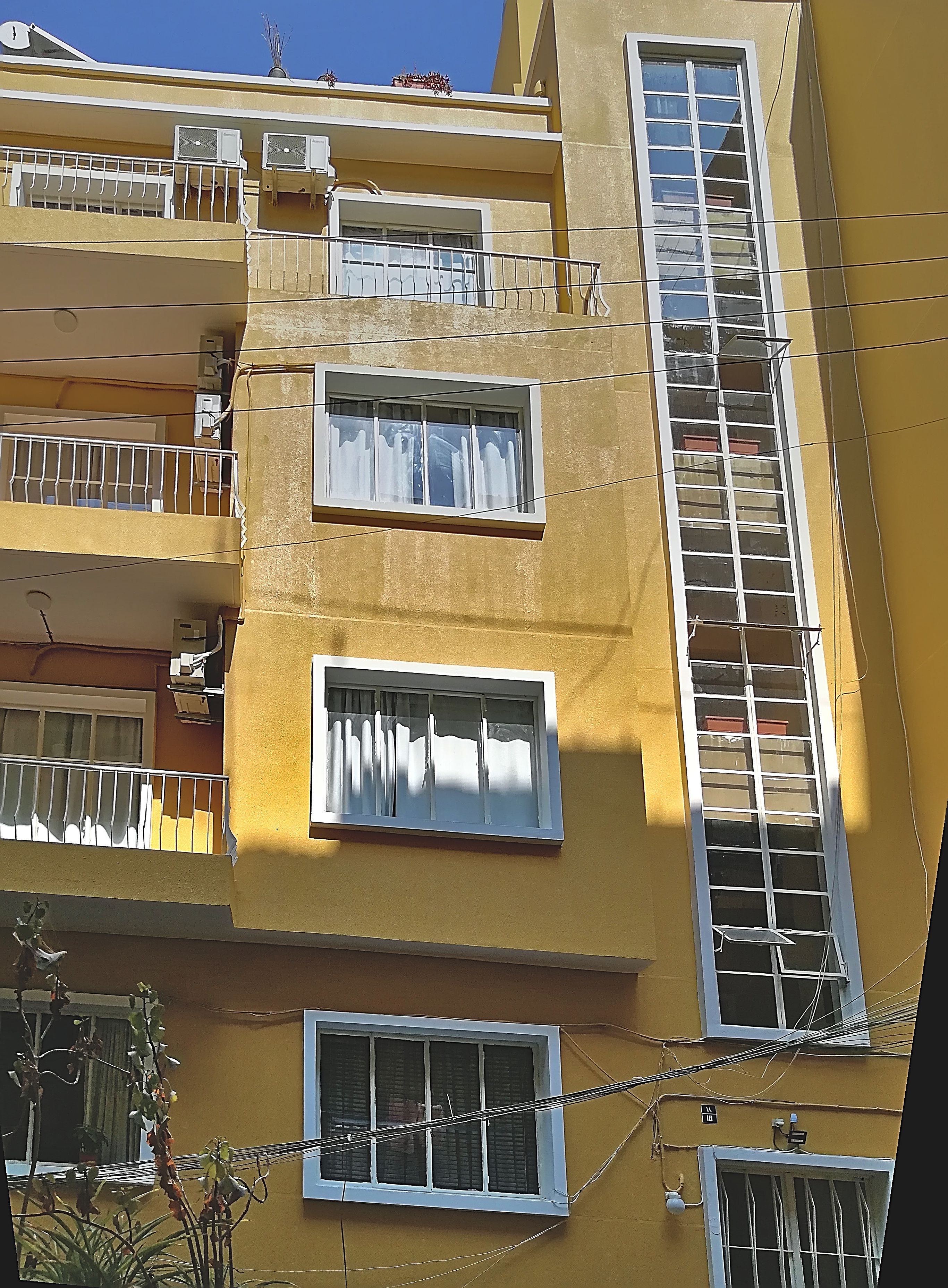 Un edificio de varios pisos con balcones, unidades de aire acondicionado y una escalera contra incendios.