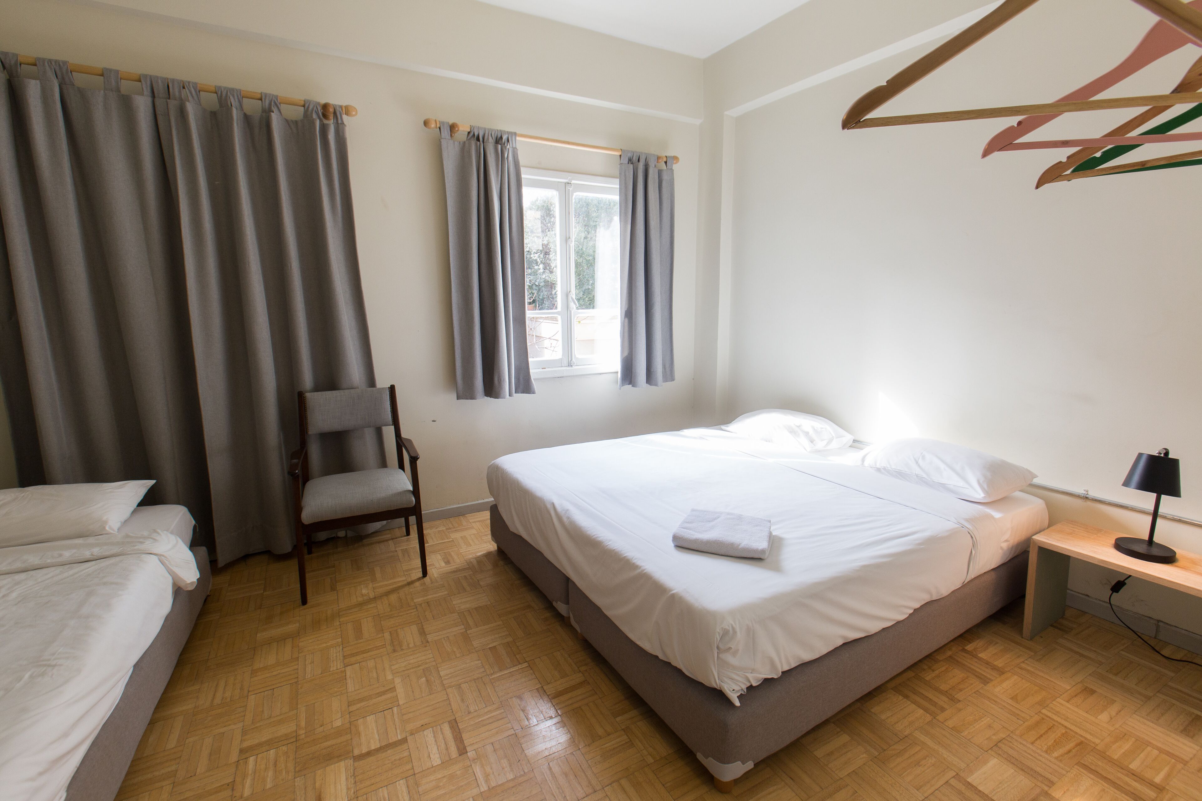 Une chambre à coucher avec un lit, une chaise, une table de chevet et une fenêtre avec des rideaux.