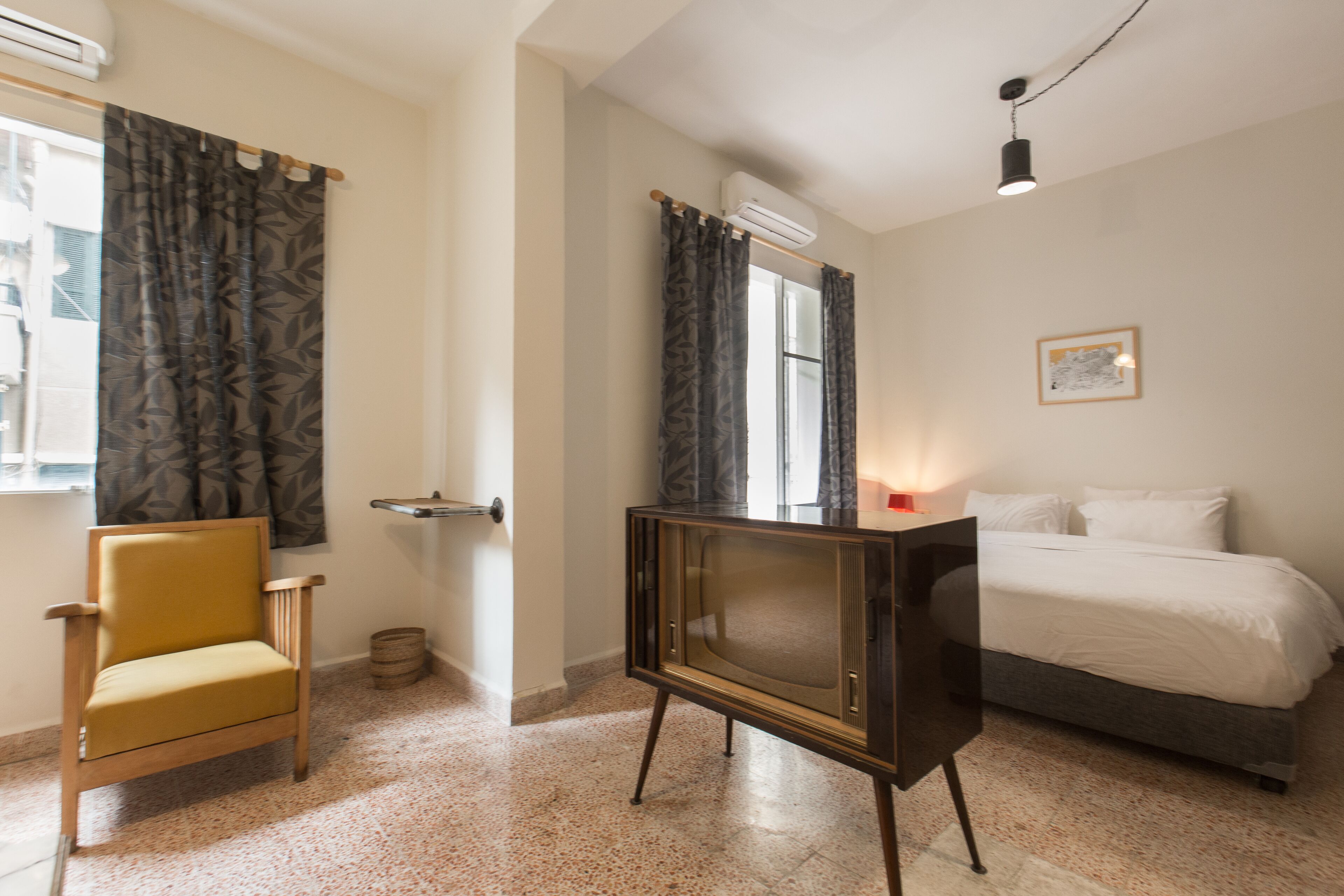A bedroom with a bed, a chair, a television, and an air conditioning unit.