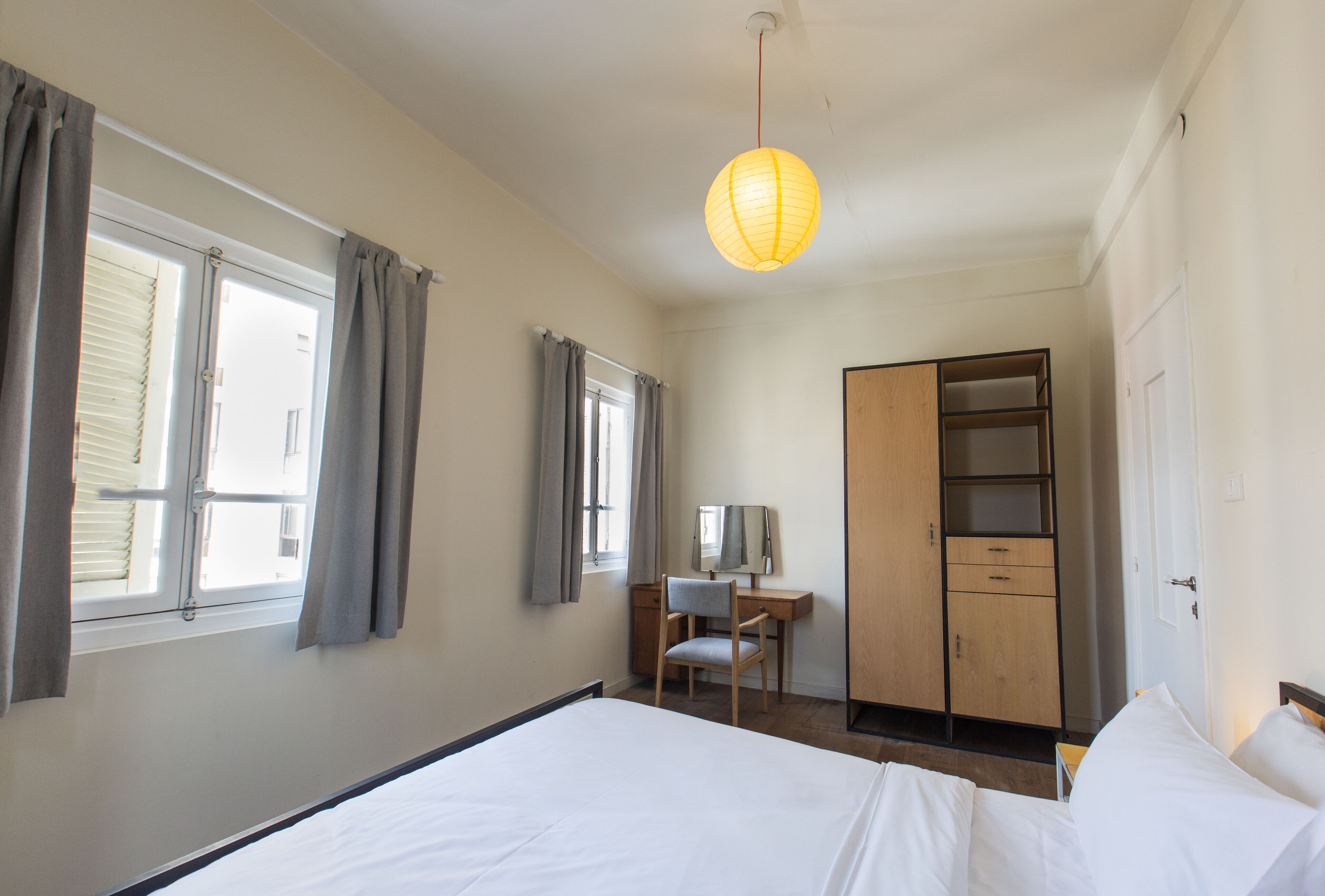 Habitación de hotel con cama, escritorio y silla, armario y una lámpara colgante.