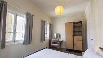 A hotel room with a bed, a desk with a chair, a wardrobe, and a hanging light fixture.