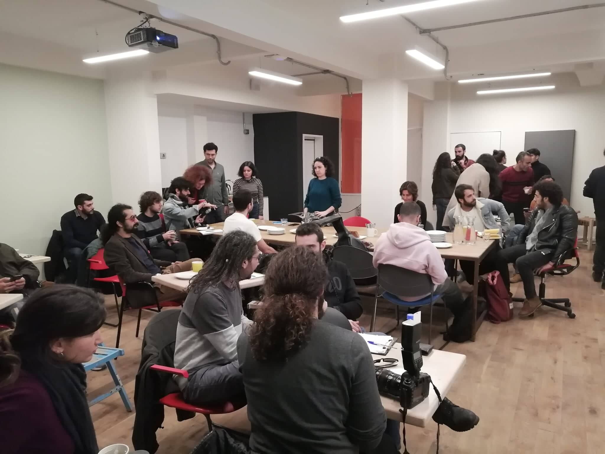 A conference room with round tables, attendees seated, and a speaker at the front.