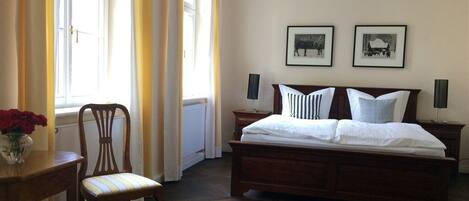 Un dormitorio con una cama de madera, dos mesitas de noche, una silla y un ventanal con cortinas.