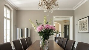 A dining room with a long wooden table, six chairs, a vase of flowers, a chandelier, and framed artwork on the wall. - Herrenhaus Röddelin (Templin)